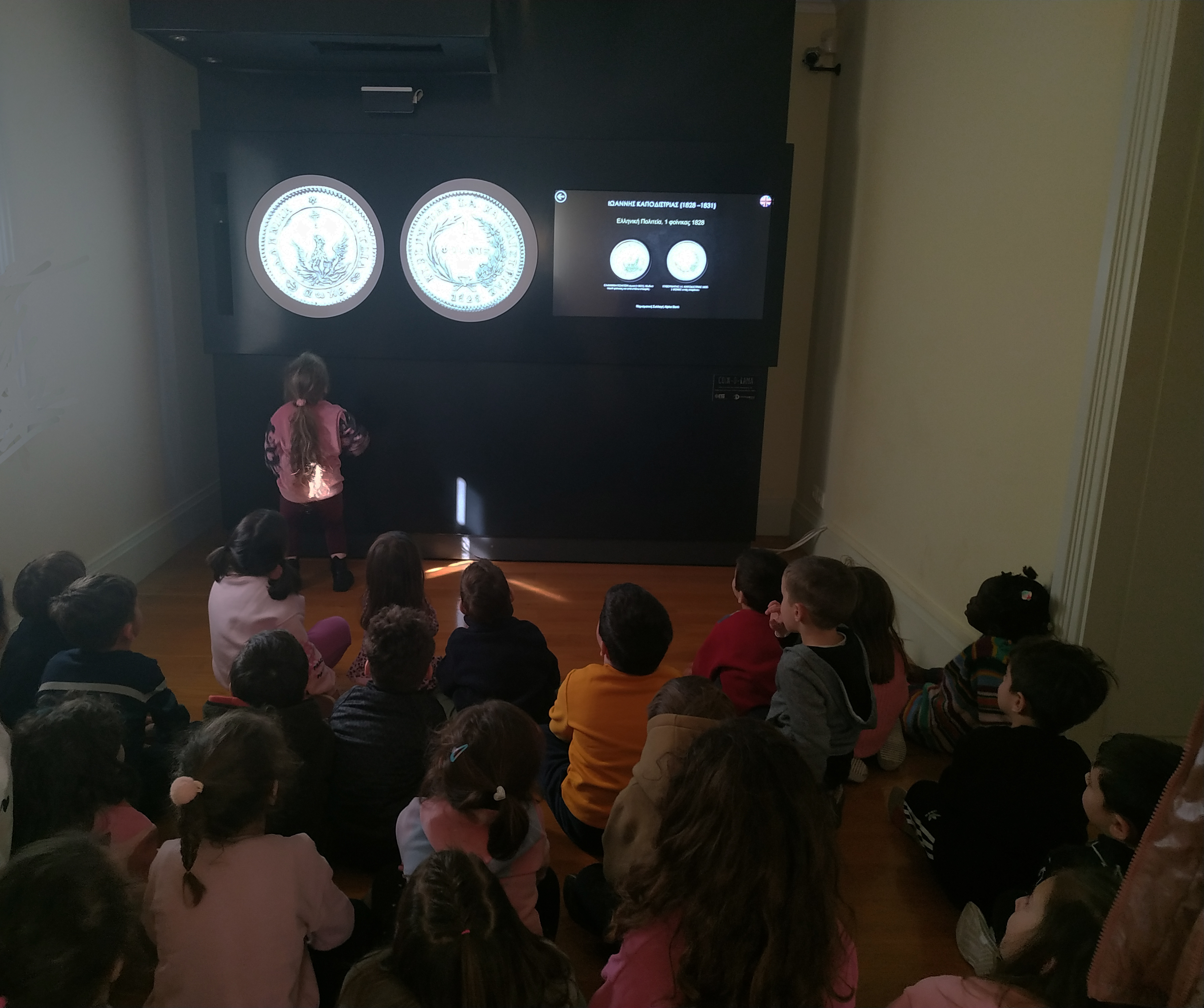 Group of young visitors around a banknote display case watching the tour.  Highlight from the tour at the Ionian Bank