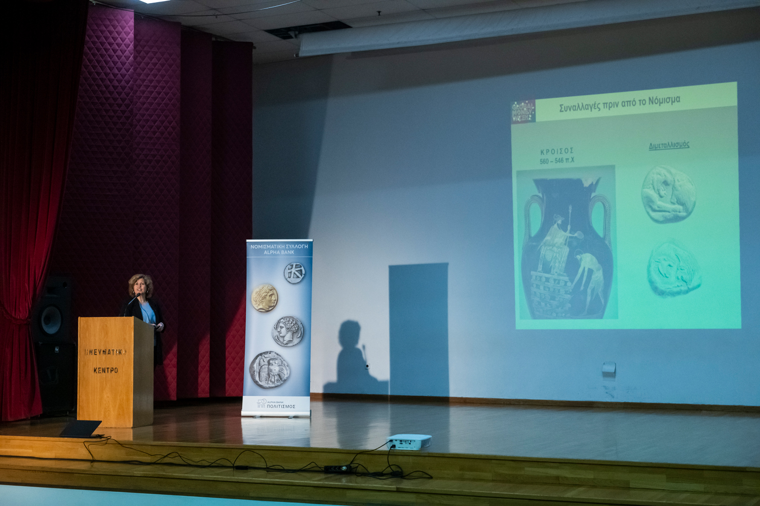 Αριστερά η Δρ Δήμητρα Τσαγκάρη στο βήμα, δεξιά παρουσίαση σε προβολέα. Παρουσίαση στο Κυριακοπούλειο Πολιτιστικό Κέντρο Ιτέας