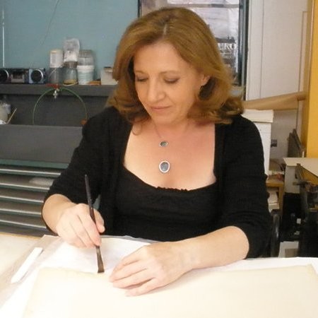 The bookbinder is holding a brush and working on white paper. Evangelia Biza