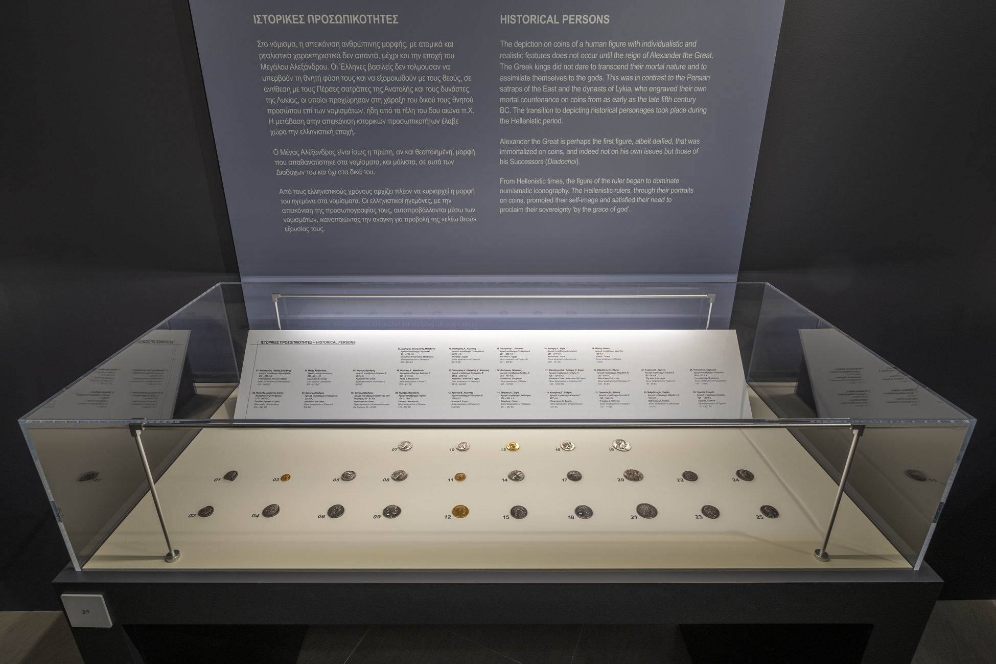 Γυάλινη προθήκη με χρυσά και ασημένια νομίσματα, και από πάνω μπλε αφίσα με πληροφορίες.  Έκθεση «Η άλλη όψη του νομίσματος»