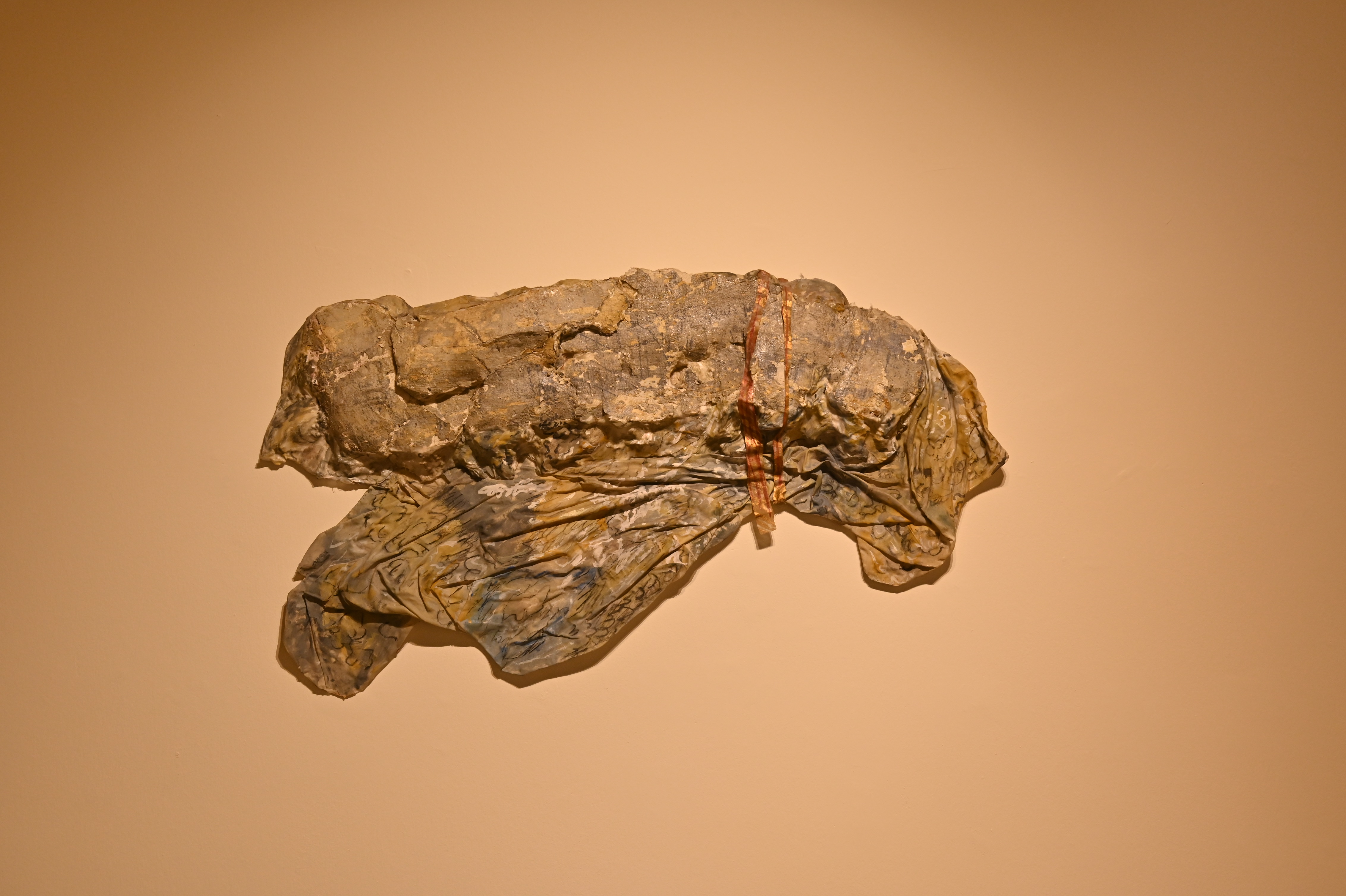 Αποτοιχισμένη επιφάνεια ακανόνιστου σχήματος σε αποχρώσεις του γκρι και της ώχρας, τοποθετημένο σε τοίχο.  Baalbeks της Ρένας Παπασπύρου