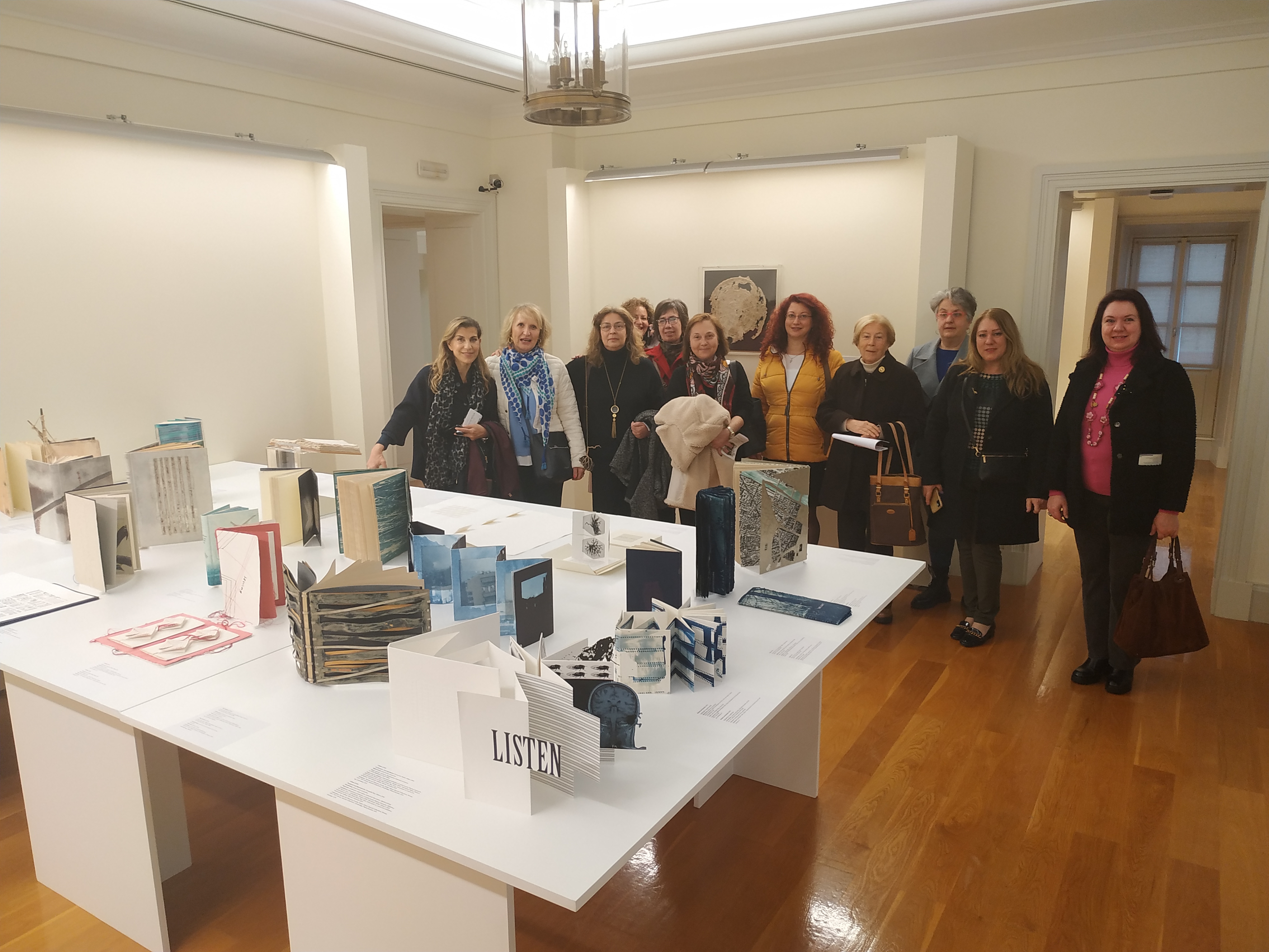 Women-members of the Corfu Soroptimist Club behind a table with works by Evangelia Biza. Group photo from the visit