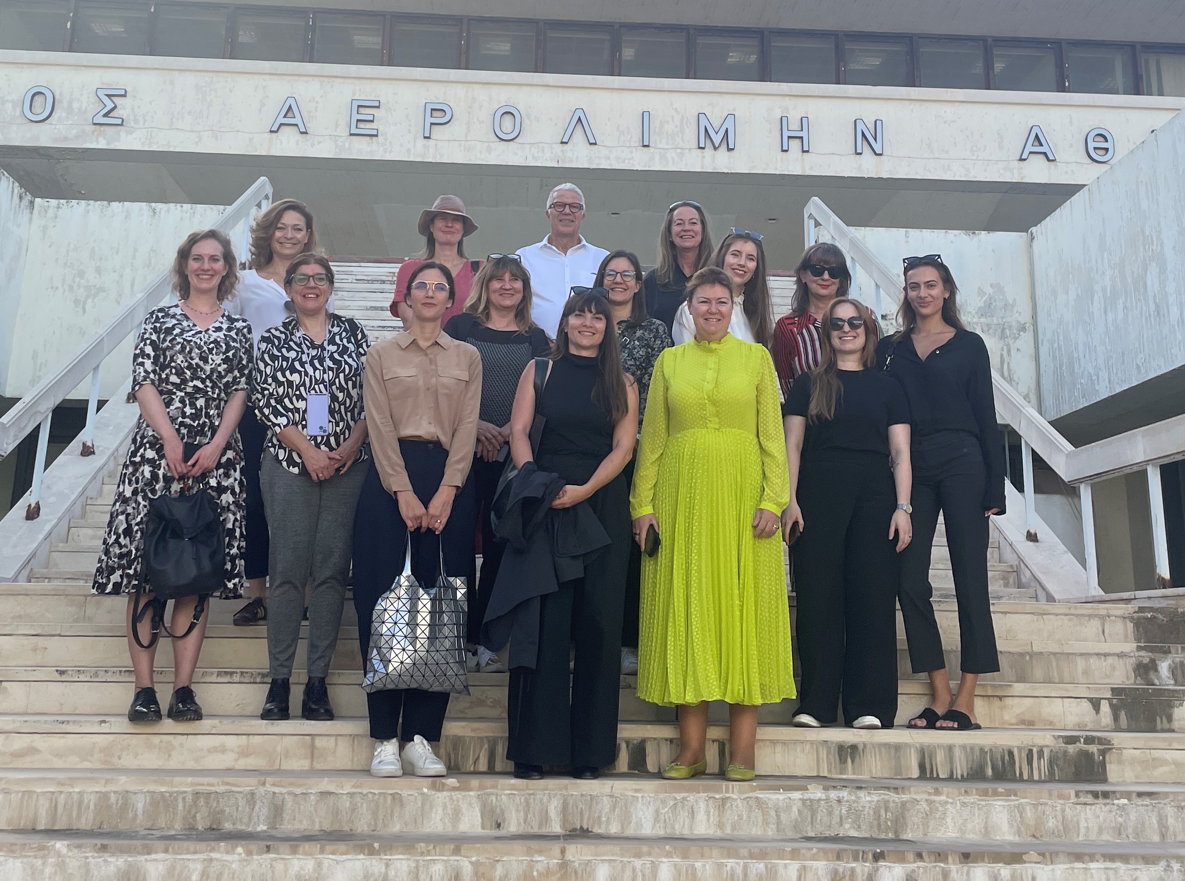 Άνδρας και γυναίκες στέκονται σε σκάλα μπροστά από κτίριο του παλιού αεροδρομίου στο Ελληνικό. Συνάντηση μελών IACCCA στην Αθήνα