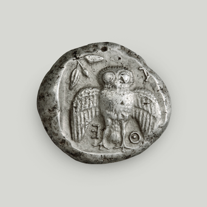 Reverse of Athenian silver tetradrachm depicting an owl with spread wings; the legend reads ATHE.  Reverse of Athenian silver decadrachm